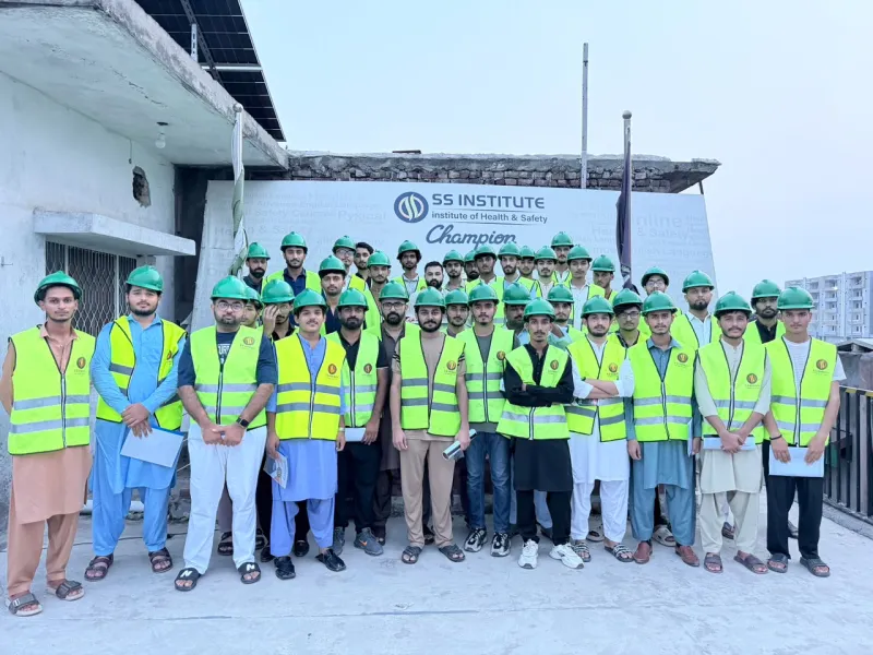 ایس ایس انسٹیٹیوٹ کے بینر کے سامنے ہیلمٹ اور حفاظتی جیکٹ پہنے طلبہ